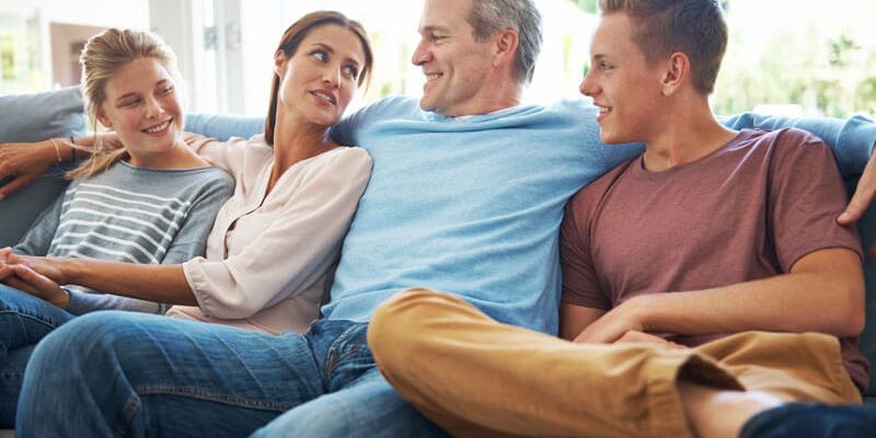 Zwei Jugendliche sitzen entspannt mit ihren Eltern auf der Couch